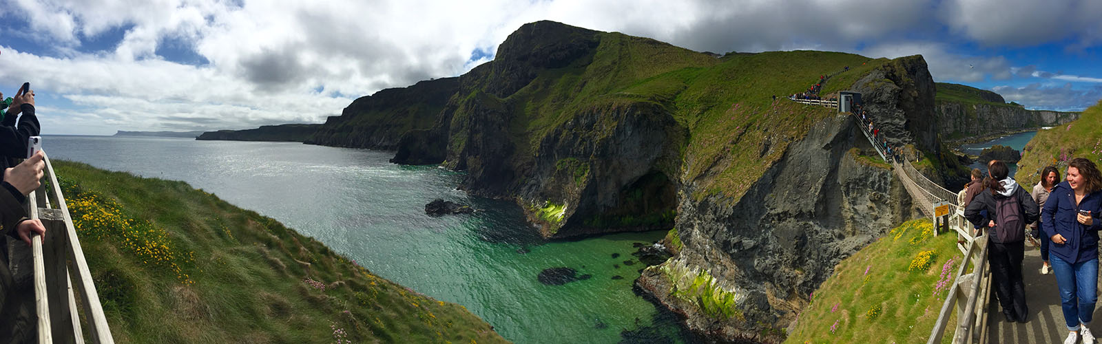A narrow wooden bridge hangs between two rocky cliffs, overlooking the turquoise water below. 